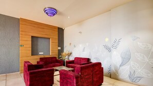 A reception area with red sofas, a wooden accent wall, a wall-mounted light fixture, and a floral wall design. - Deluxe Matoshree Palace (Satara)
