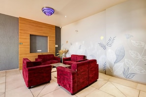 A reception area with red sofas, a wooden accent wall, a wall-mounted light fixture, and a floral wall design.