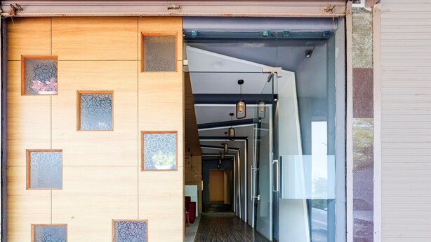 A hallway with a wooden wall and glass doors, leading to a room with a bed and a red chair. - Deluxe Matoshree Palace (Satara)