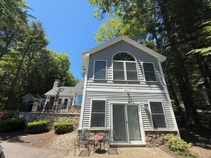 A two-story house with a stone foundation, large windows, and a patio with outdoor furniture.