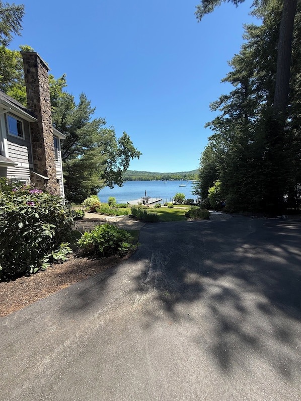 A house with a stone chimney, a paved driveway, and a view of a lake with boats.