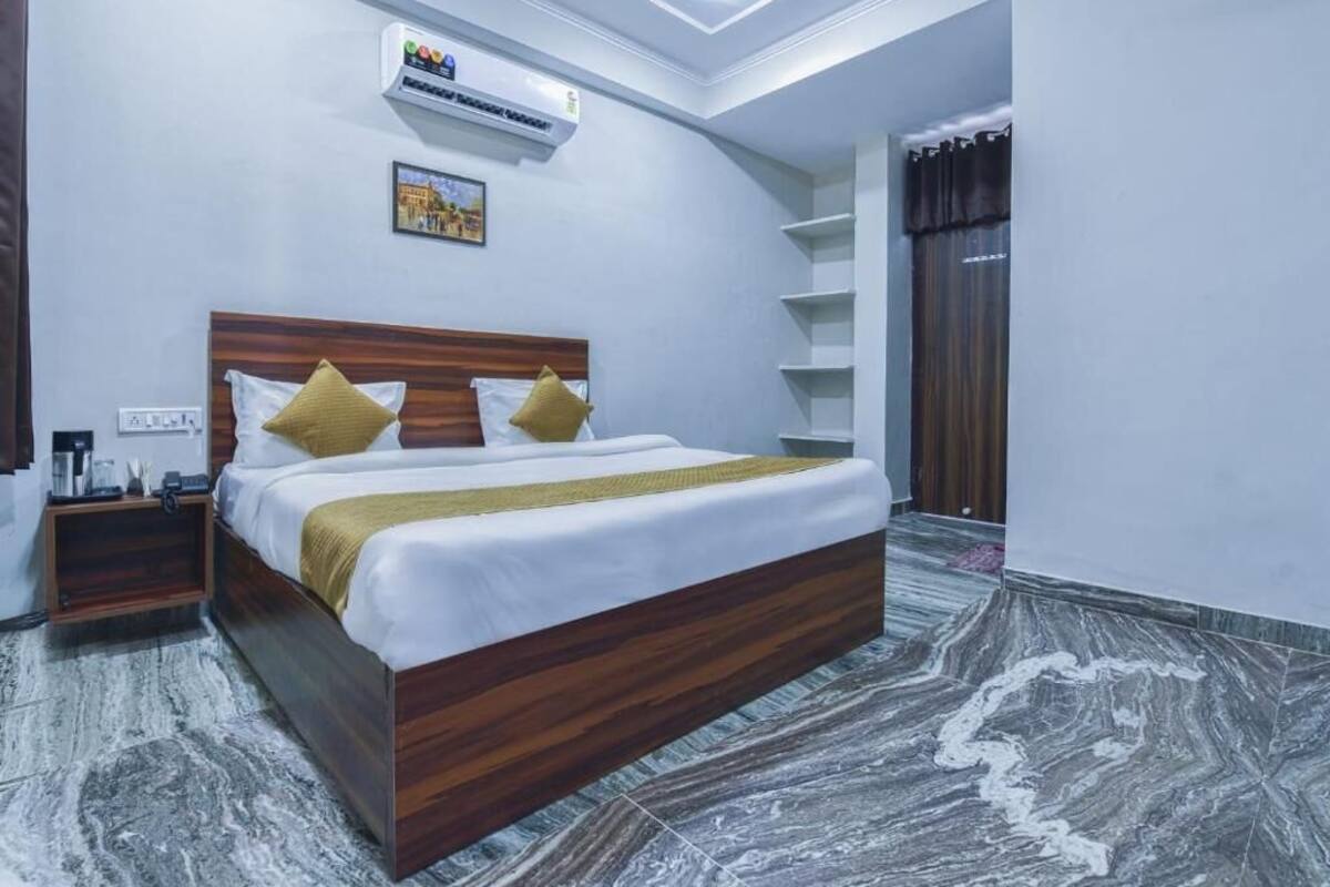 Habitación de hotel con cama de madera, ropa blanca de cama, una mesita de noche pequeña, aire acondicionado de pared y un cuadro.