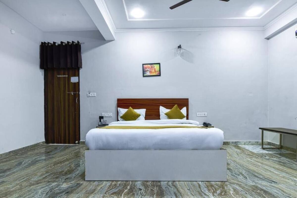 Habitación de hotel con cama, mesita de noche, ventilador de techo, lámpara de pared y puerta con cortina.