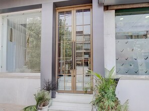 Un bâtiment avec une entrée dotée d’une porte en verre, une enseigne bien visible indiquant un magasin de téléphones portables, et des plantes en pot à l’extérieur.