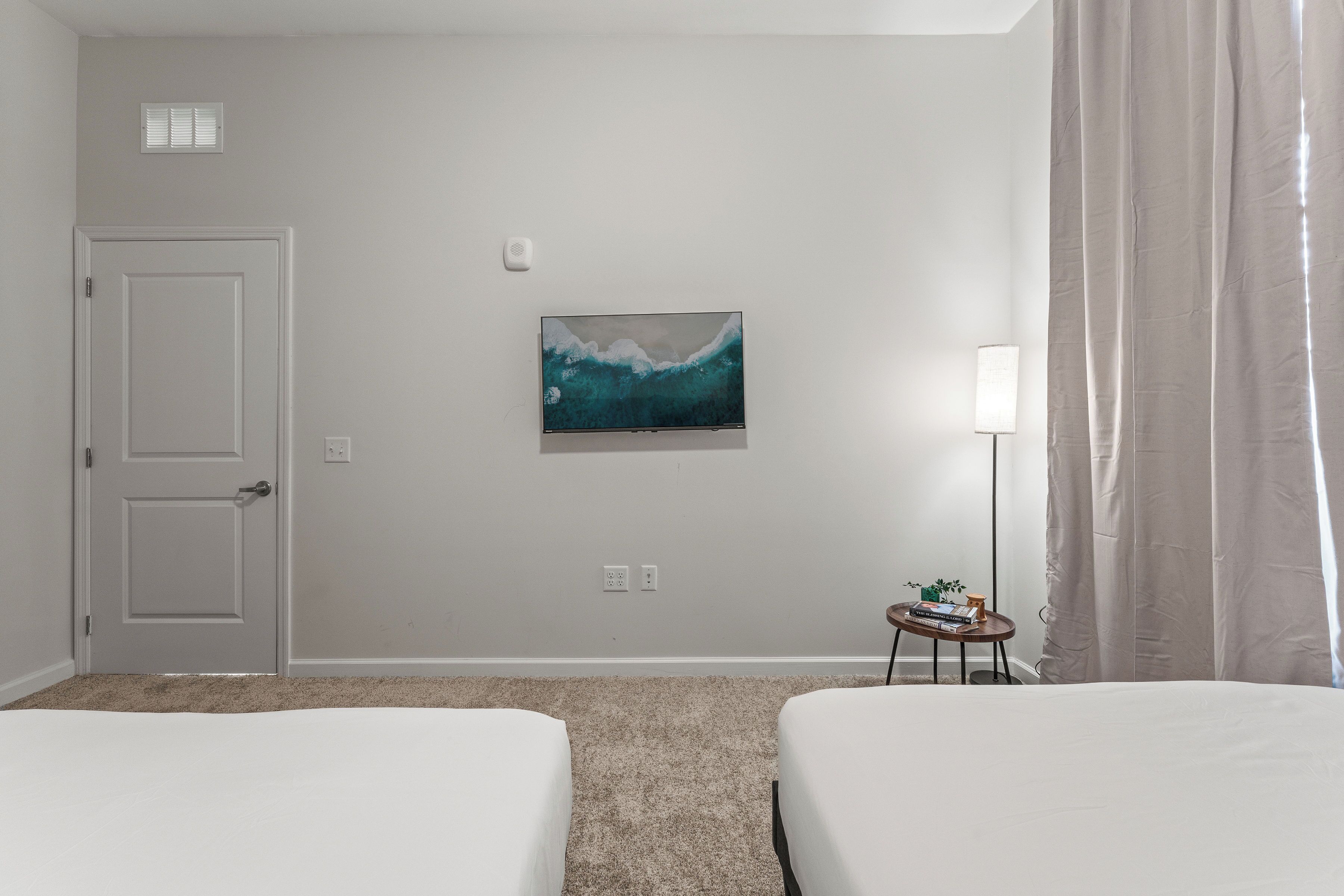 Una camera d'albergo con due letti, un quadro appeso al muro, una lampada e un tavolino con una pianta.