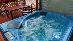 A hot tub with a control panel, surrounded by wooden furniture and a lattice fence. - Cliff Cottage Inn - Zelda King Hot Tub Suite (Eureka Springs)