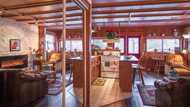 Un intérieur chaleureux avec une cheminée, des meubles en bois, un coin cuisine et de grandes fenêtres.