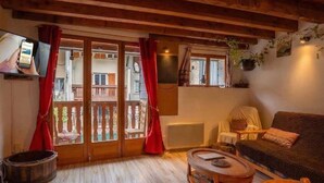 A cozy living room with a wooden ceiling, a sofa, a coffee table, and a television. - Chez Ludo I T4 I Francin (Porte-de-Savoie)