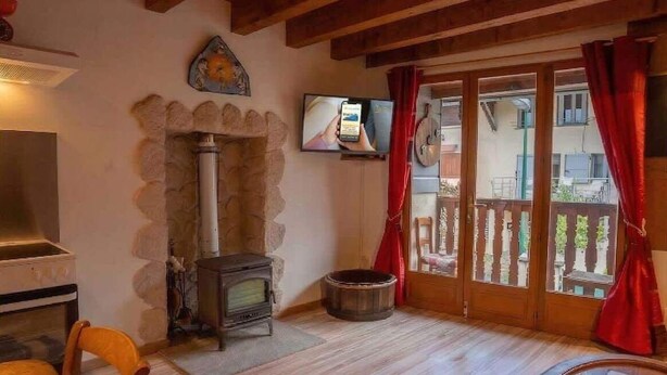 A cozy room with a stone fireplace, a television, and a wooden ceiling. - Chez Ludo I T4 I Francin (Porte-de-Savoie)
