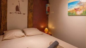 A bedroom with a wooden ceiling, a bed with two pillows, a nightstand with a lamp, and a painting on the wall. - Chez Ludo I T4 I Francin (Porte-de-Savoie)