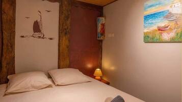 Ein Schlafzimmer mit Holzbalkendecke, einem Bett mit zwei Kissen, einem Nachttisch mit Lampe und einem Gemälde an der Wand.
