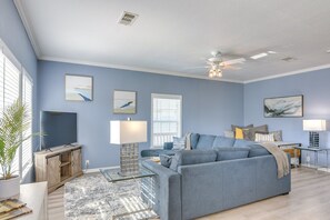 A living room with a blue sofa, a TV, a fireplace, and artwork on the walls. - Beautiful 3-bedroom house with Hot Tub in charming Crystal Beach (Crystal Beach)