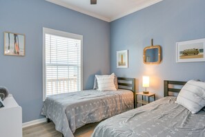 A bedroom with two beds, a window with blinds, a bedside table with a lamp, and wall art. - Beautiful 3-bedroom house with Hot Tub in charming Crystal Beach (Crystal Beach)