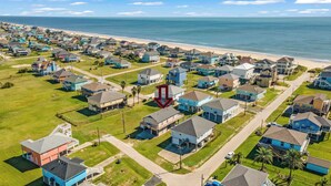 Vista aérea de una zona residencial costera con casas, una playa y un cielo despejado.
