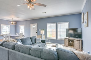 A living room with a sectional sofa, a TV, a ceiling fan, and a dining area with a table and chairs. - Beautiful 3-bedroom house with Hot Tub in charming Crystal Beach (Crystal Beach)