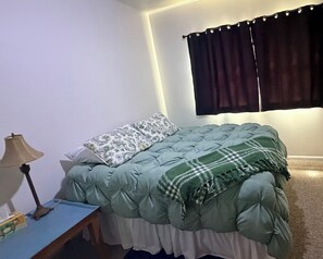 Una camera da letto con un letto, un comodino, una lampada e una finestra con tende.