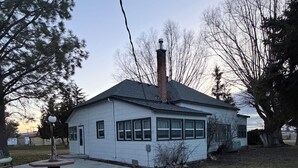 Una casa de un piso con chimenea, un porche delantero y una entrada de vehículos visible.