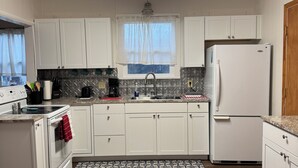 Una cocina moderna con armarios blancos, un lavamanos de acero inoxidable, un refrigerador blanco y un salpicadero con diseño.