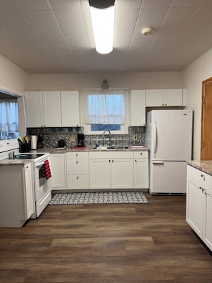 A modern kitchen with white cabinets, a stainless steel sink, a white refrigerator, and a patterned backsplash.