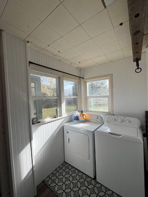 A laundry room with two washing machines, a drying rack, and a window with a view of the outdoors.