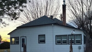Una casa de una sola planta con chimenea, un porche con banca y una pequeña mesa exterior.