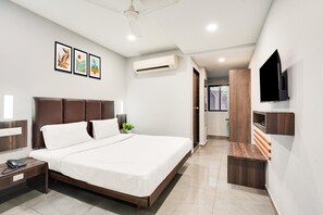 A modern hotel room with a large bed, bedside tables, a flat-screen TV, and artwork on the wall. - Deluxe Country Club (Surat)