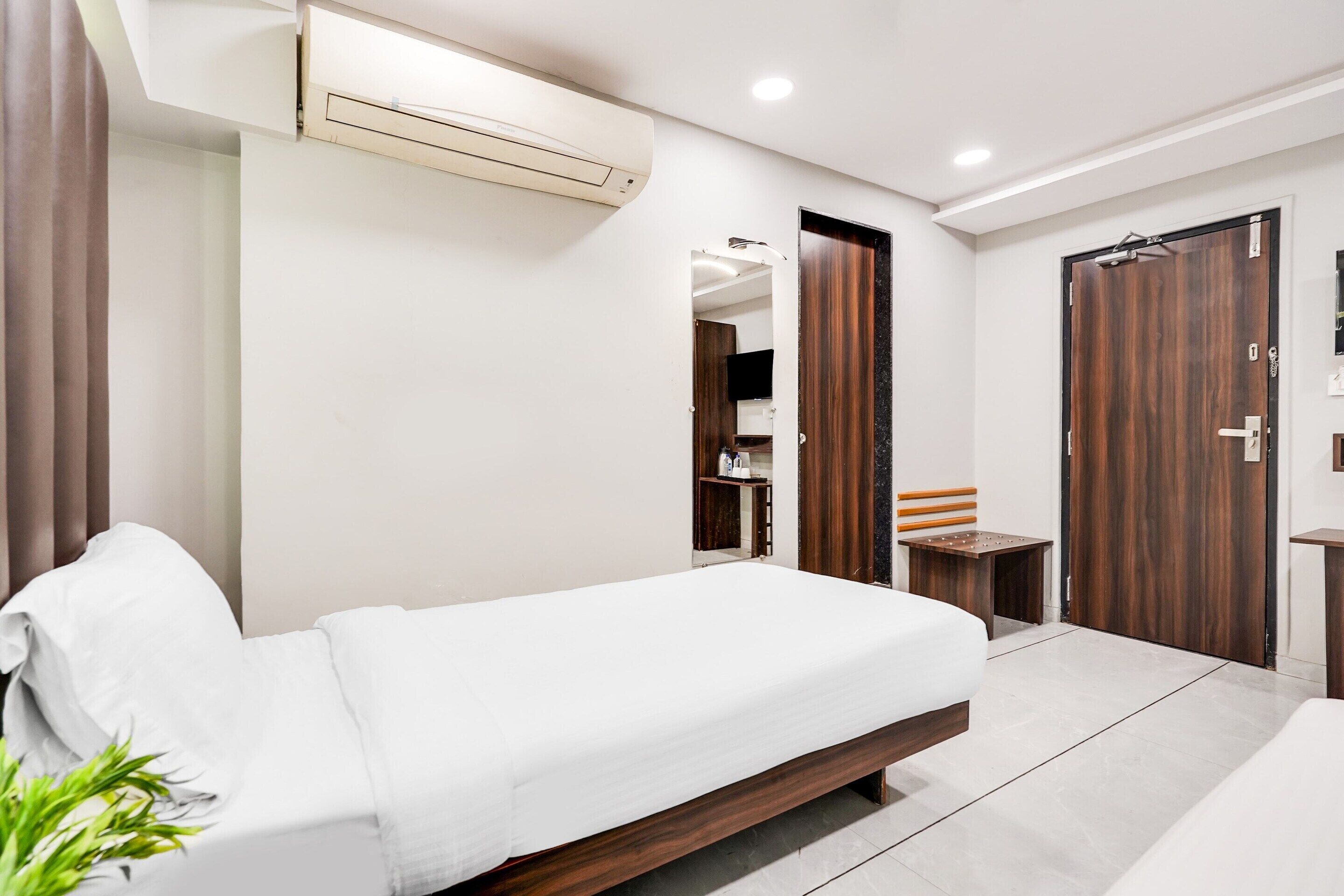 A modern bedroom with a bed, a small table, a wardrobe, and an air conditioning unit.
