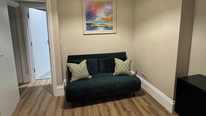 Una habitación con un sofá verde oscuro, un cuadro en la pared y una lámpara de techo a rayas.
