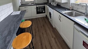 Una cocina compacta con armarios blancos, horno empotrado, lavadora y un lavamanos. Hay dos taburetes de madera en la encimera.