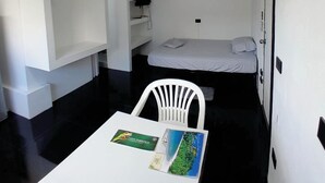A compact room with a bed, a white chair, a small table with a map, and a ceiling fan. - Costa Rica Walk In (San José)