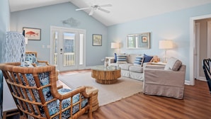 A living room with a ceiling fan, a wicker chair, a round coffee table, a sofa, and a door leading outside. - Charming 4BR Cottage | Walk to Beach | Outdoor Space | Atlantic Beach (Atlantic Beach)