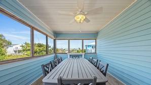 A covered outdoor dining area with a table and chairs, large windows, and a ceiling fan. - Charming 4BR Cottage | Walk to Beach | Outdoor Space | Atlantic Beach (Atlantic Beach)
