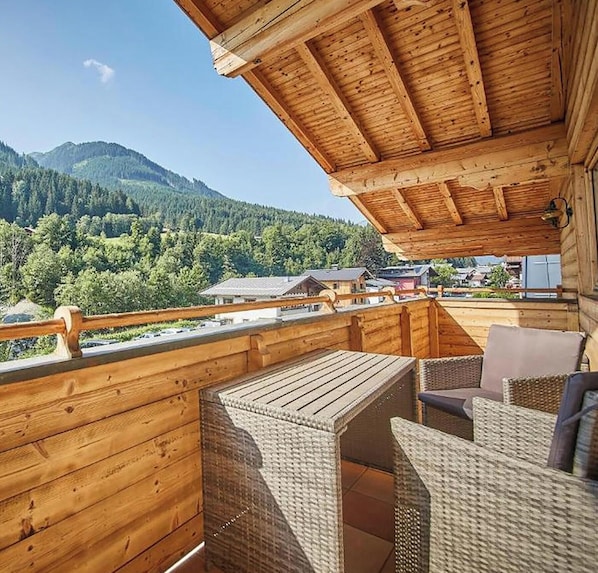 A wooden balcony with wicker furniture, overlooking a mountainous landscape. - Appartement Haus Alexander (Saalbach)