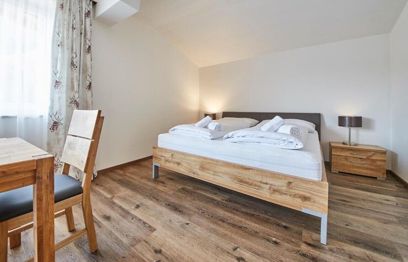 Een slaapkamer met een houten bed, een nachtkastje, een stoel en een bureau.