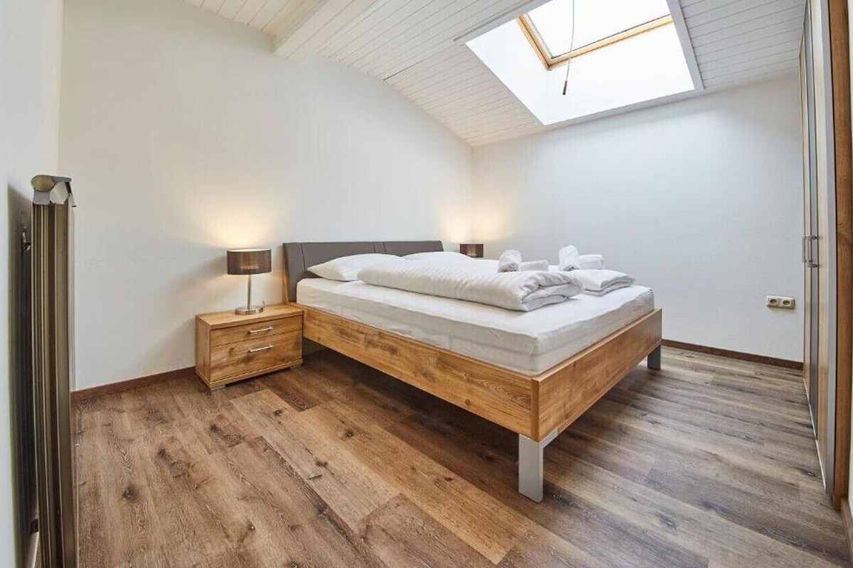 A bedroom with a skylight, a wooden bed, bedside tables, and a nightstand.