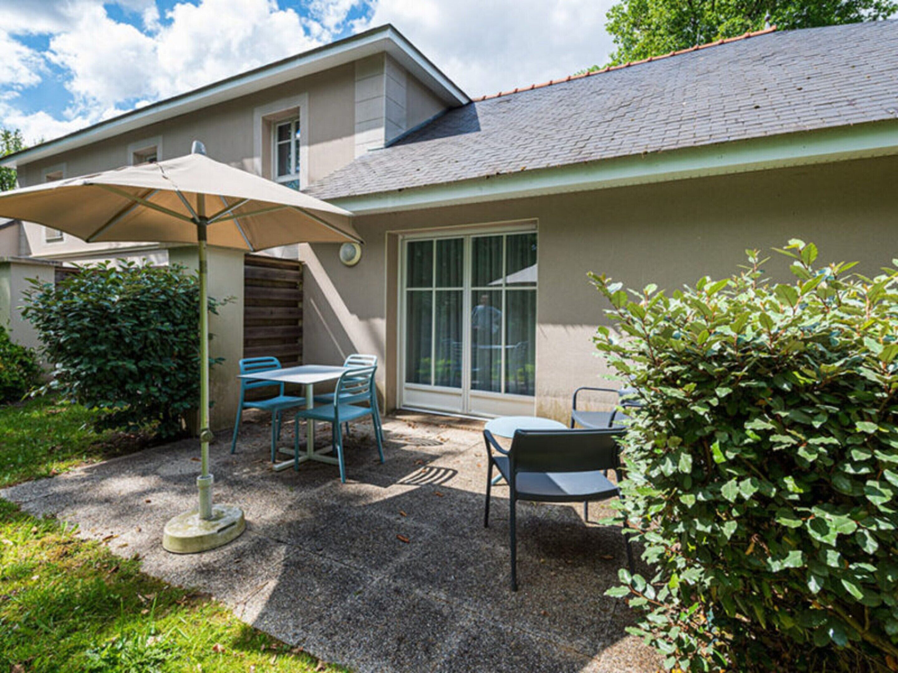 A patio with a table and chairs, a covered umbrella, and a window.