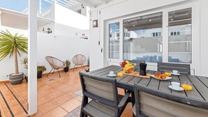 Un patio con una mesa dispuesta para el desayuno, incluyendo cruasanes y fruta, y dos sillas.