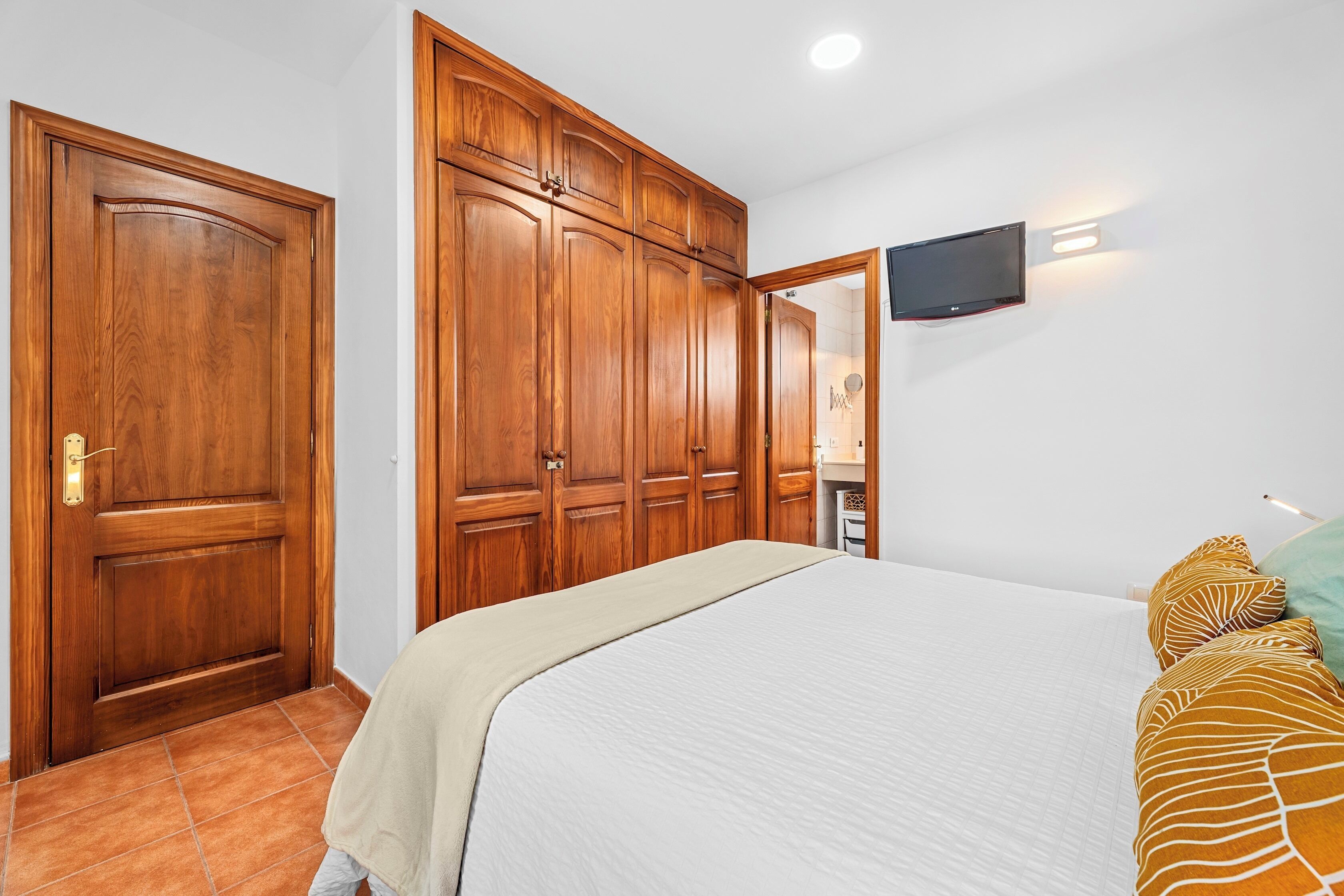 Een slaapkamer met een bed, een houten kledingkast en een tv aan de muur.