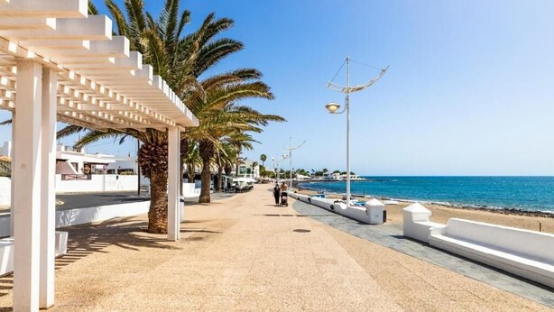 Un paseo marítimo con una pérgola blanca, palmeras y una vista despejada del océano.
