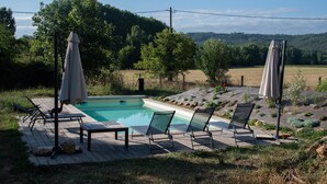 A swimming pool with lounge chairs and umbrellas, surrounded by a landscaped garden and a view of a forested hill. - THE FARM: 145m2, 6 pers-3 bedrooms swimming pool/river/isolated/ Montignac Lascaux at 9.2km (Saint-Léon-sur-Vézère)