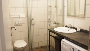 Ein Badezimmer mit Glasdusche, Toilette, Waschbecken mit Spiegel und einer Waschmaschine.