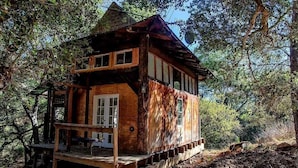 A wooden cabin with a porch, large windows, and a staircase leading to the entrance.