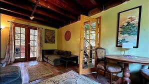 A cozy room with a wooden ceiling, a dining table, a sofa, and a large window.