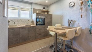 A modern kitchen with grey cabinets, a built-in oven, a dining table with chairs, and a clock on the wall. - Vacation apartment in a quiet location, not far from the sandy beach (Crikvenica)