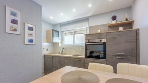 A modern kitchen with a dining area, featuring a built-in oven, a sink, and a window above the counter. - Vacation apartment in a quiet location, not far from the sandy beach (Crikvenica)