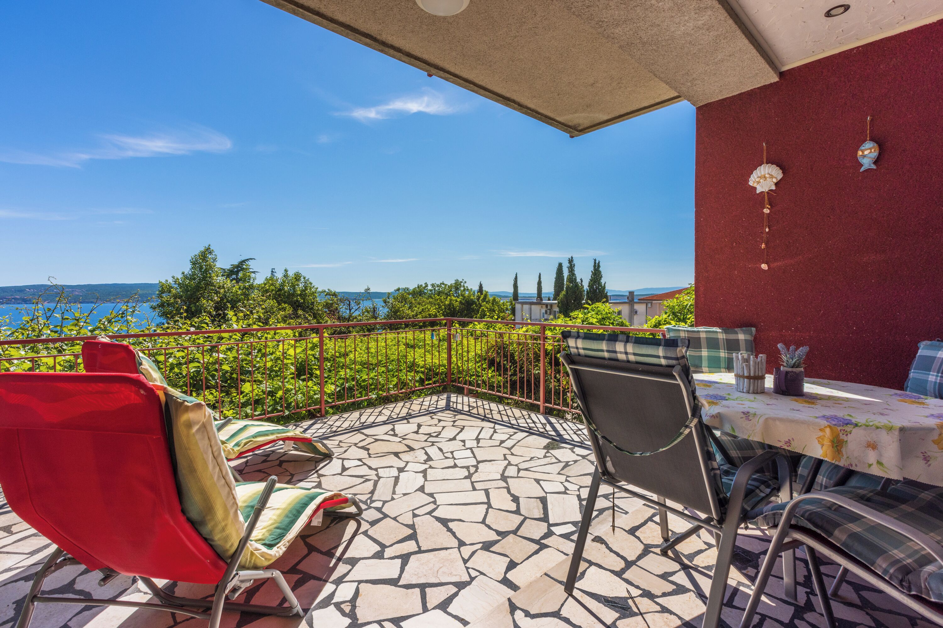 A terrace with a stone floor, red railing, and a table with a floral tablecloth.