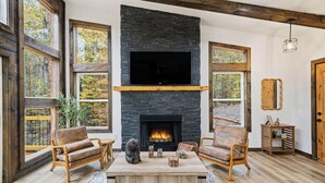 A living room with a stone fireplace, wooden furniture, and large windows. - Serene Ellijay Getaway with Coffee Bar, Two Fireplaces, Hot Tub, Games  + Resort (Ellijay)