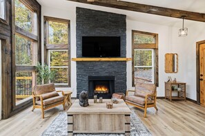 Ein Wohnzimmer mit Kamin aus Stein, Holzmöbeln und großen Fenstern.