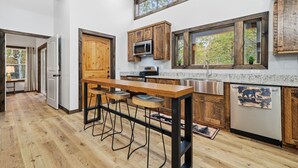 A modern kitchen with wooden cabinets, a bar stool area, and a large window. - Serene Ellijay Getaway with Coffee Bar, Two Fireplaces, Hot Tub, Games  + Resort (Ellijay)