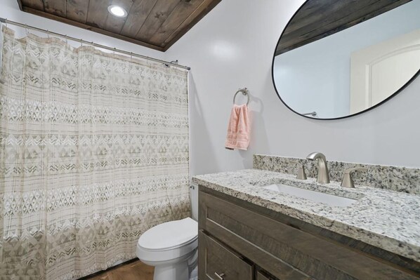 A bathroom with a shower curtain, toilet, sink with a mirror, and a towel hanging on the wall. - Serene Ellijay Getaway with Coffee Bar, Two Fireplaces, Hot Tub, Games + Resort (Ellijay)